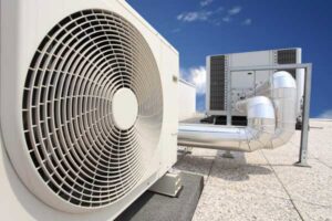 An outdoor AC unit fan with a large rooftop HVAC system in the background by Glendale HVAC in Glendale, AZ