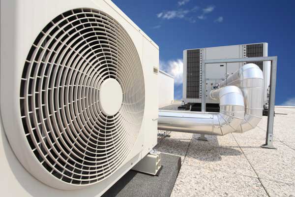 An outdoor AC unit fan with a large rooftop HVAC system in the background by Glendale HVAC in Glendale, AZ