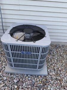 An outdoor air conditioning unit installed on a gravel bed next to a building by Preferred Heating & Air in Bismarck, ND.