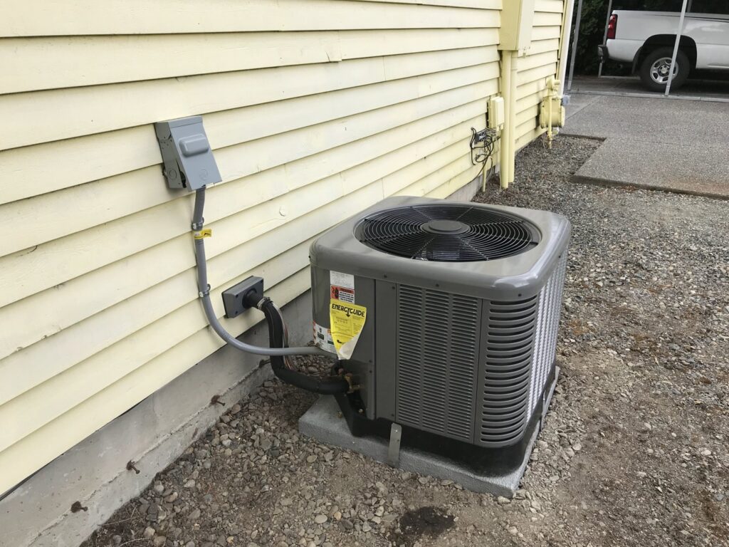 An outdoor air conditioning unit installed next to a yellow house by Columbia Heating & Air Conditioning in Kent, WA.