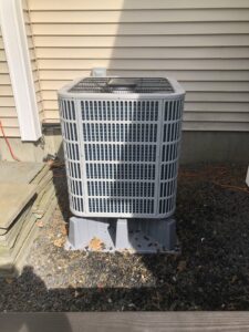 An outdoor air conditioning unit installed on a gravel bed next to a residential building by Garrison City HVACR in Dover, NH