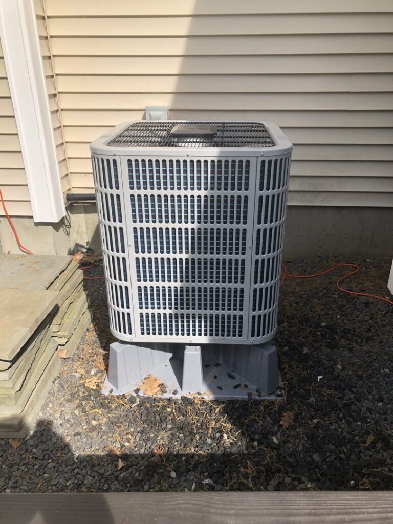 An outdoor air conditioning unit installed on a gravel bed next to a residential building by Garrison City HVACR in Dover, NH