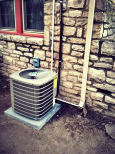 An outdoor AC unit newly installed next to a stone wall by Griffin's Heating & Air in Tulsa, OK.