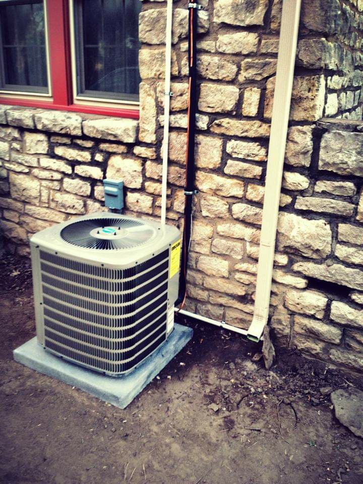 An outdoor AC unit newly installed next to a stone wall by Griffin's Heating & Air in Tulsa, OK.
