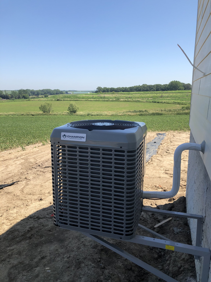 An outdoor Champion AC unit installed next to a new home with a rural landscape by Air Care in Sioux Falls, SD.