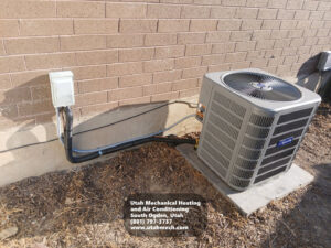 An outdoor AC unit installation next to a brick wall by Utah Mechanical Heating and Air Conditioning in South Ogden, UT.