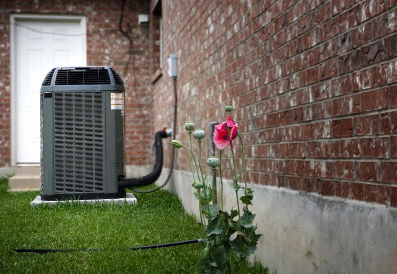 An outdoor air conditioning unit installed next to a brick house by Missouri River Heating & Cooling in Mandan, ND.