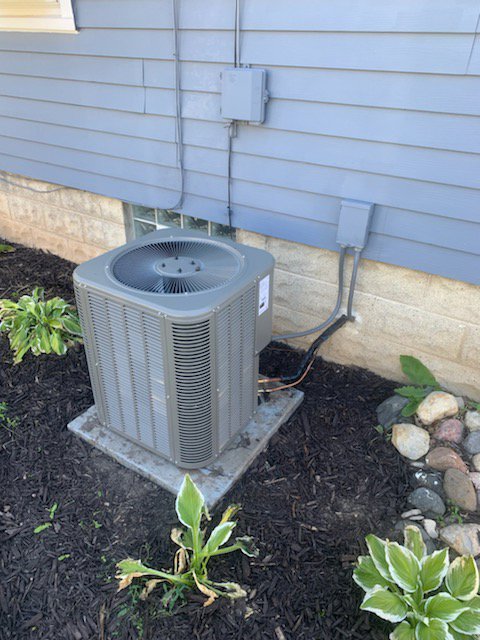 An outdoor air conditioning unit surrounded by landscaping, installed by Heating and Cooling Drs of Waukesha, Pewaukee, and Delafield, Waukesha, WI.