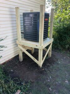An outdoor AC unit installed on a custom wooden stand by Griffin's Heating & Air in Tulsa, OK.
