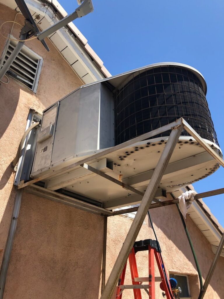 An outdoor air conditioning unit mounted on a platform on the side of a building, serviced by Ace A/C & Heating in Henderson, NV.