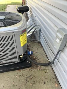 An outdoor air conditioning unit with refrigerant lines and electrical disconnect installed by Specialized Service Heat & Air in Wichita, KS.