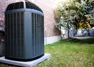 An outdoor air conditioning unit next to a brick house, serviced by Reid Plumbing & Heating in Manhattan, KS.