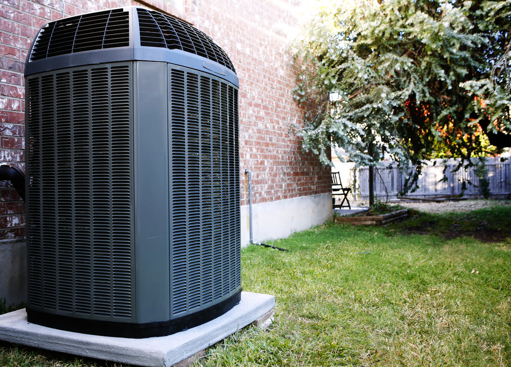 An outdoor air conditioning unit next to a brick house, serviced by Reid Plumbing & Heating in Manhattan, KS.