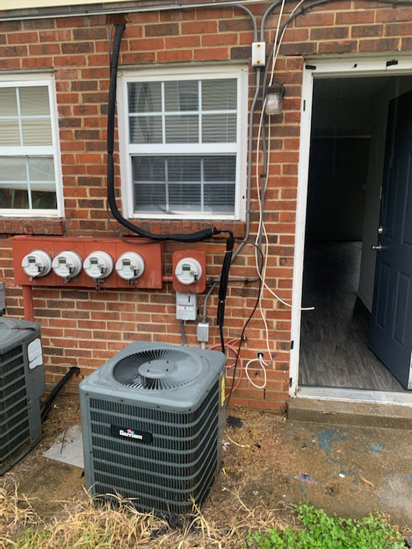 An outdoor AC unit installed next to a brick residential building by Air Energy Solutions in North Chesterfield, VA