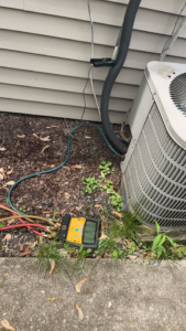 An HVAC technician servicing an outdoor air conditioning unit with gauges for Affordable Heating & Cooling in Lafayette, IN.