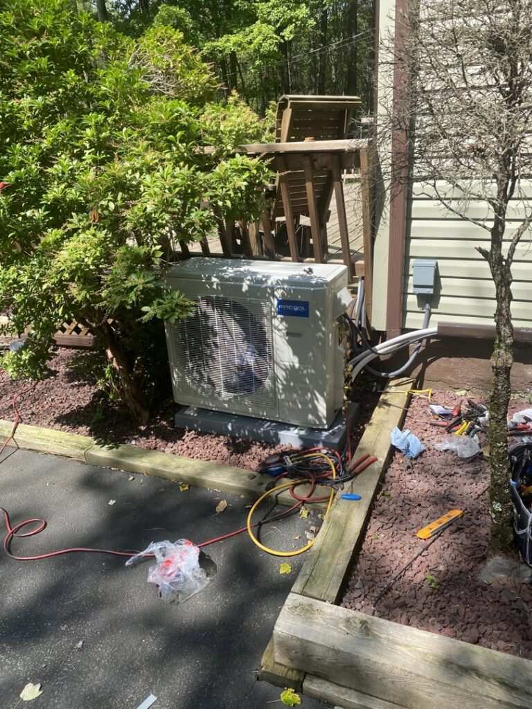 An outdoor AC unit being serviced with tools and lines on the ground by Kane Heating & Air in Mountain Top, PA.
