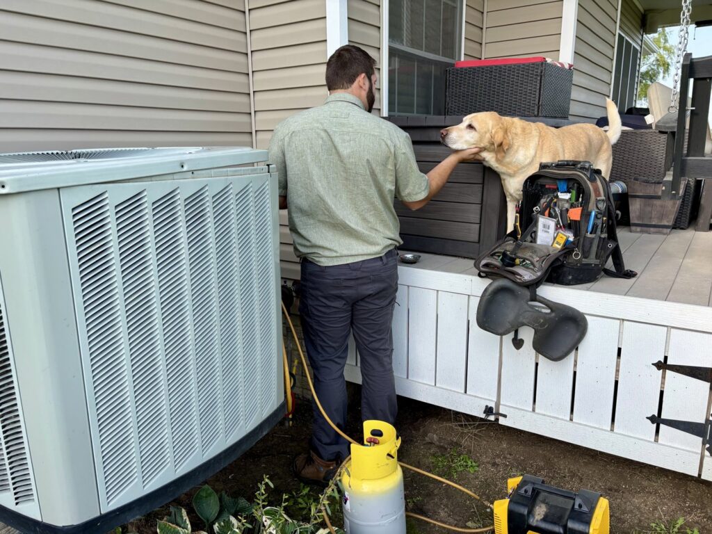 An HVAC technician servicing an outdoor AC unit with refrigerant tanks for Polar Air Heating and Cooling in Omaha, NE