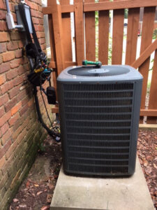 An outdoor air conditioning unit next to a brick wall with tools, indicating service by West Tennessee Heat & Air in Memphis, TN