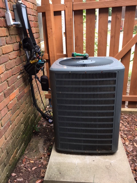 An outdoor air conditioning unit next to a brick wall with tools, indicating service by West Tennessee Heat & Air in Memphis, TN