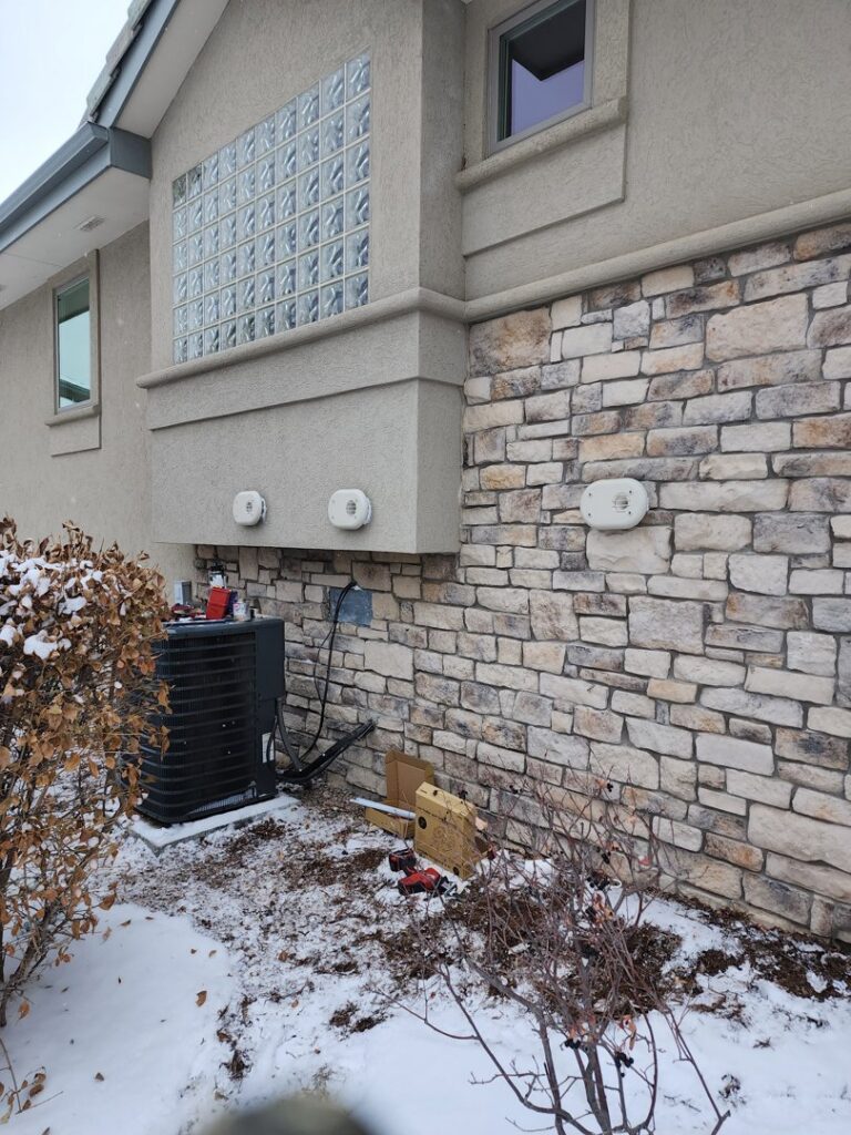 An outdoor air conditioning unit being serviced or installed during winter by D & D Heating & Air in Brighton, CO.