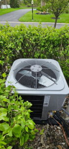 An outdoor air conditioning unit surrounded by green bushes, installed by Empire Heating & Air Conditioning in Decatur, GA