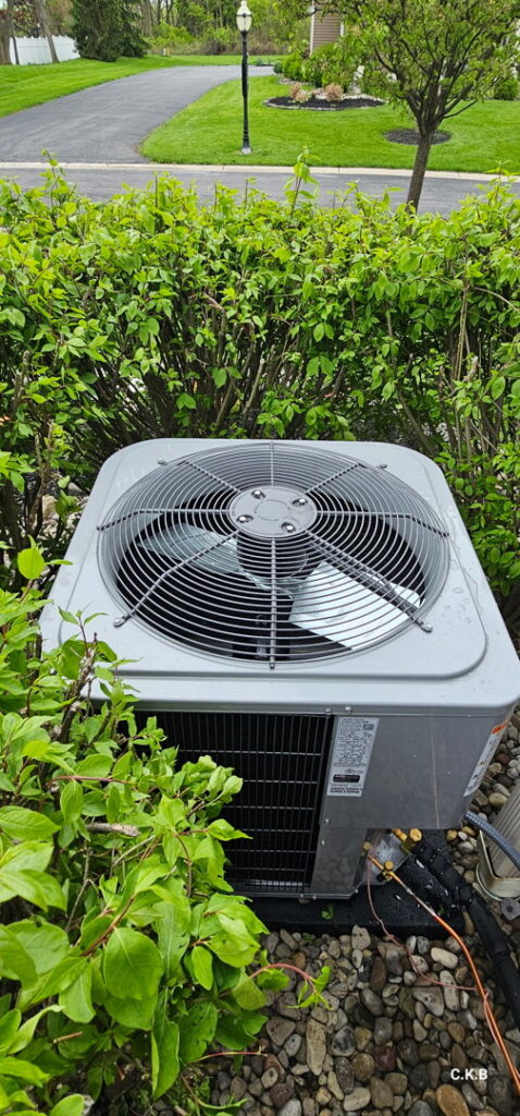 An outdoor air conditioning unit surrounded by green bushes, installed by Empire Heating & Air Conditioning in Decatur, GA