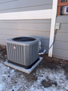 An outdoor air conditioning unit next to a house in winter, serviced by Nexus Heating & Air in Denver, CO.