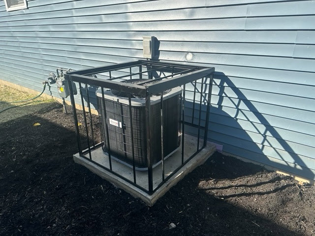 An outdoor AC unit with a protective metal cage installed by Fellowship Heating and Cooling in Indianapolis, IN.