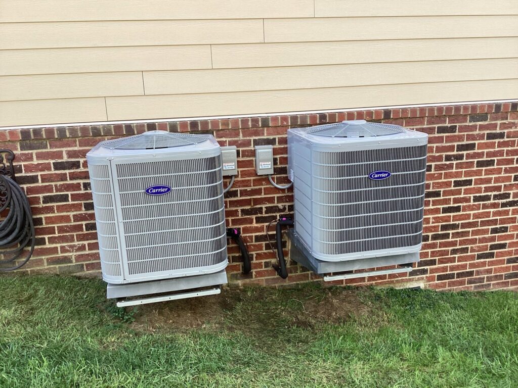 Two Carrier outdoor AC units installed next to a brick house by Advanced HVAC and Plumbing in Morgantown, WV.