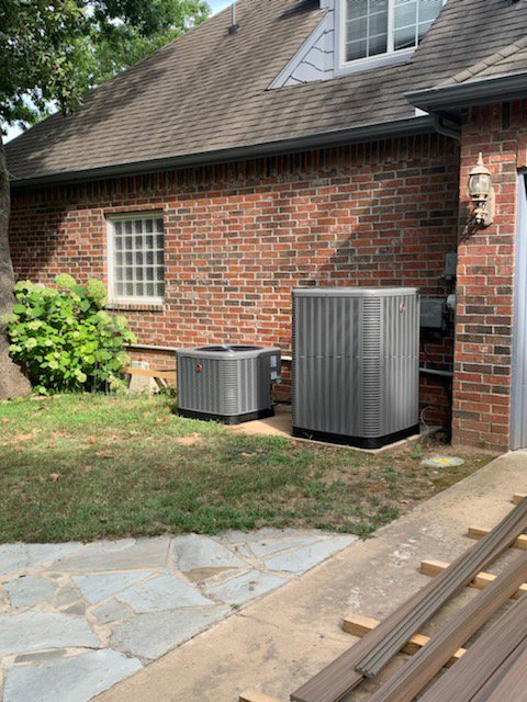Two outdoor air conditioning units installed next to a brick residential home by Dowd Heat & Air in Tulsa, OK.
