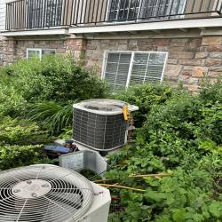 Two outdoor air conditioning units, one obscured by overgrown bushes, serviced by EPIC Heating and Air in Loveland, CO
