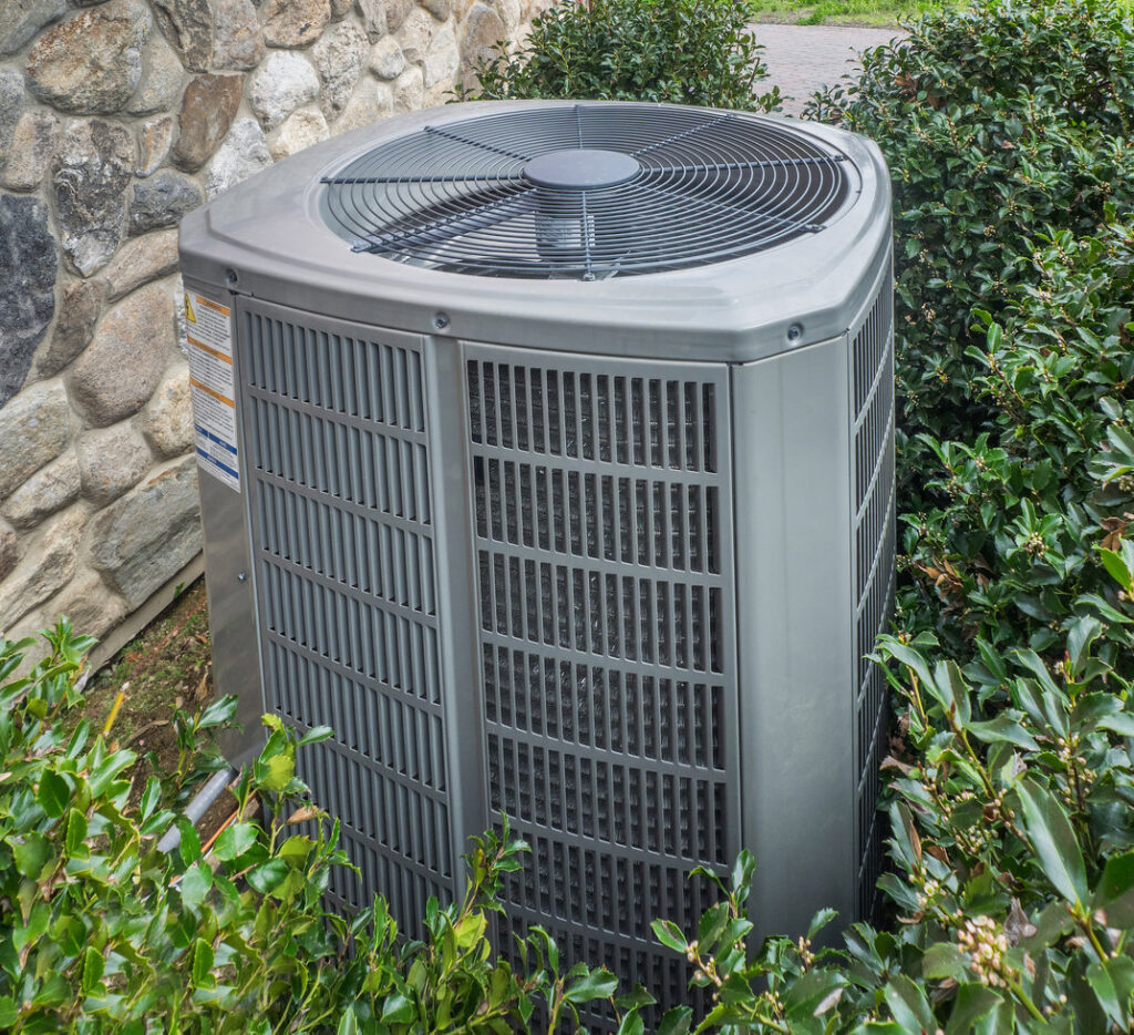 An outdoor air conditioner condenser unit installed next to a stone wall by C & C Temp Control in Worcester, MA.
