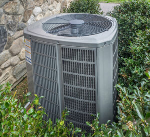 An outdoor air conditioner condenser unit installed next to a stone wall by C & C Temp Control in Worcester, MA.