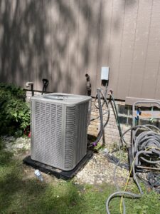An outdoor air conditioning condenser unit installed next to a residential building by Crain Heating and Cooling in Jeffersonville, IN.
