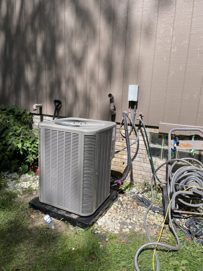 An outdoor air conditioning condenser unit installed next to a residential building by Crain Heating and Cooling in Jeffersonville, IN.