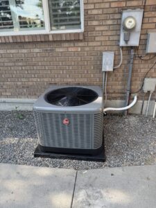 An outdoor air conditioner unit installed next to a brick wall by Peterson Heating & Cooling in Mound City, KS.