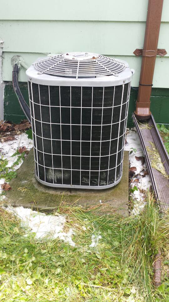 An outdoor air conditioning condenser unit next to a residential building by Cheaper Plumbing & Heating in Lansing, MI