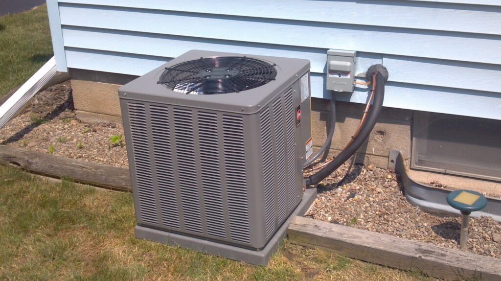 An outdoor air conditioning condenser unit installed by Huether Heating & Cooling Inc next to a home in Rochester, NY.