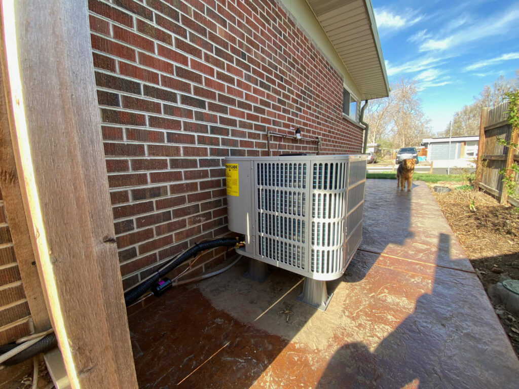 An outdoor air conditioning unit installed next to a brick home by Comfy Cave Heating and Air Conditioning in Arvada, CO.