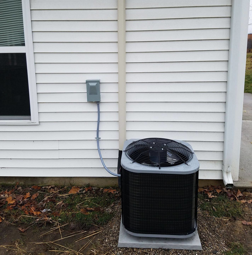 An outdoor air conditioning unit installed next to a residential home by Manz Heating and Cooling in Fort Wayne, IN.