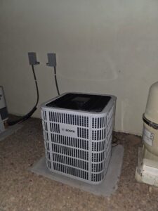 A new outdoor Bosch air conditioner condenser unit installed on a gravel pad by Krahn and Son Mechanical in Glendale, AZ.