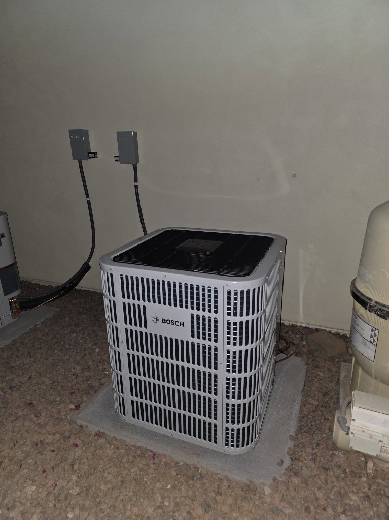 A new outdoor Bosch air conditioner condenser unit installed on a gravel pad by Krahn and Son Mechanical in Glendale, AZ.