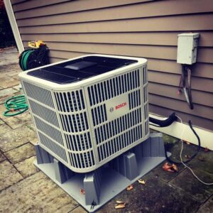 An outdoor Bosch heat pump or air conditioning unit installed next to a residential building by EML Mechanical in Boston, MA.