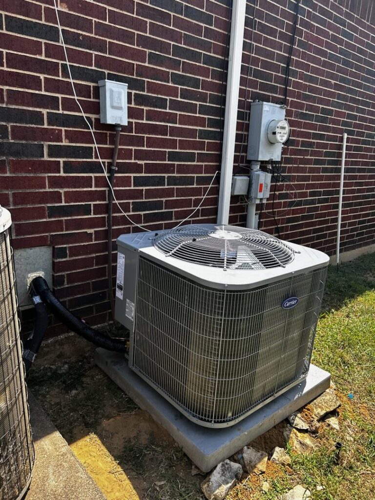 Outdoor Carrier AC unit professionally installed next to a brick wall by Benavidez Heating & Air Conditioning In, Arlington, TX.