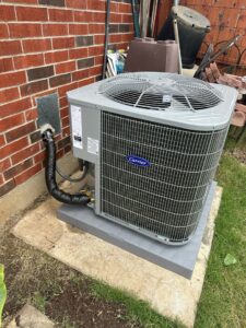 A newly installed outdoor Carrier AC unit next to a brick wall by BV Air Conditioning & Heating in Dallas, TX.