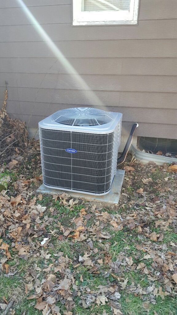 An outdoor Carrier air conditioning unit installed next to a residential building by Custom Climates in Iowa City, IA.