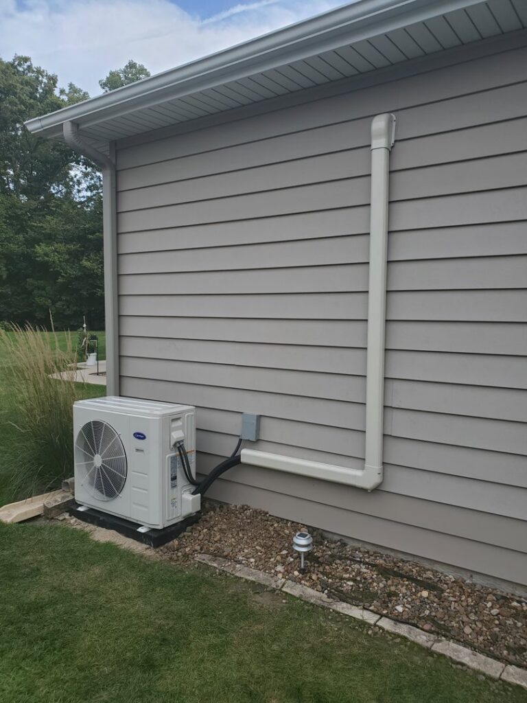 An outdoor Carrier mini-split air conditioning unit installed on the side of a house by Custom Climates in Iowa City, IA.