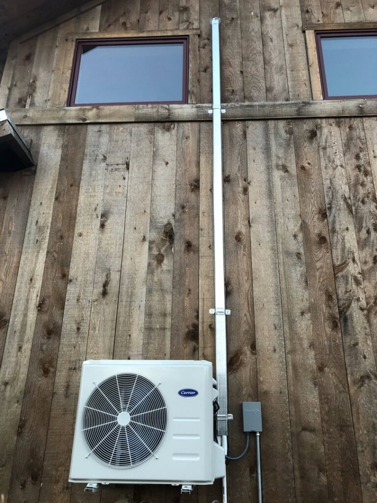 An outdoor Carrier mini-split or small commercial HVAC unit installed on a wooden building by Peterson Heating & Cooling in Mound City, KS.