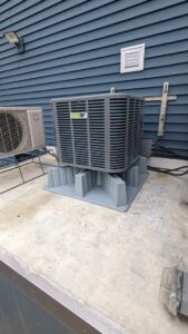 An outdoor condenser unit installed on a raised platform next to a building by WARM Global HVAC in East Providence, RI