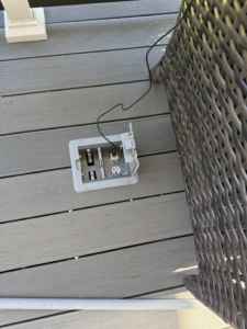 An open outdoor floor outlet with a cable plugged in on a wooden deck, installed by Watts Up Electric LLC in Summerville, SC.